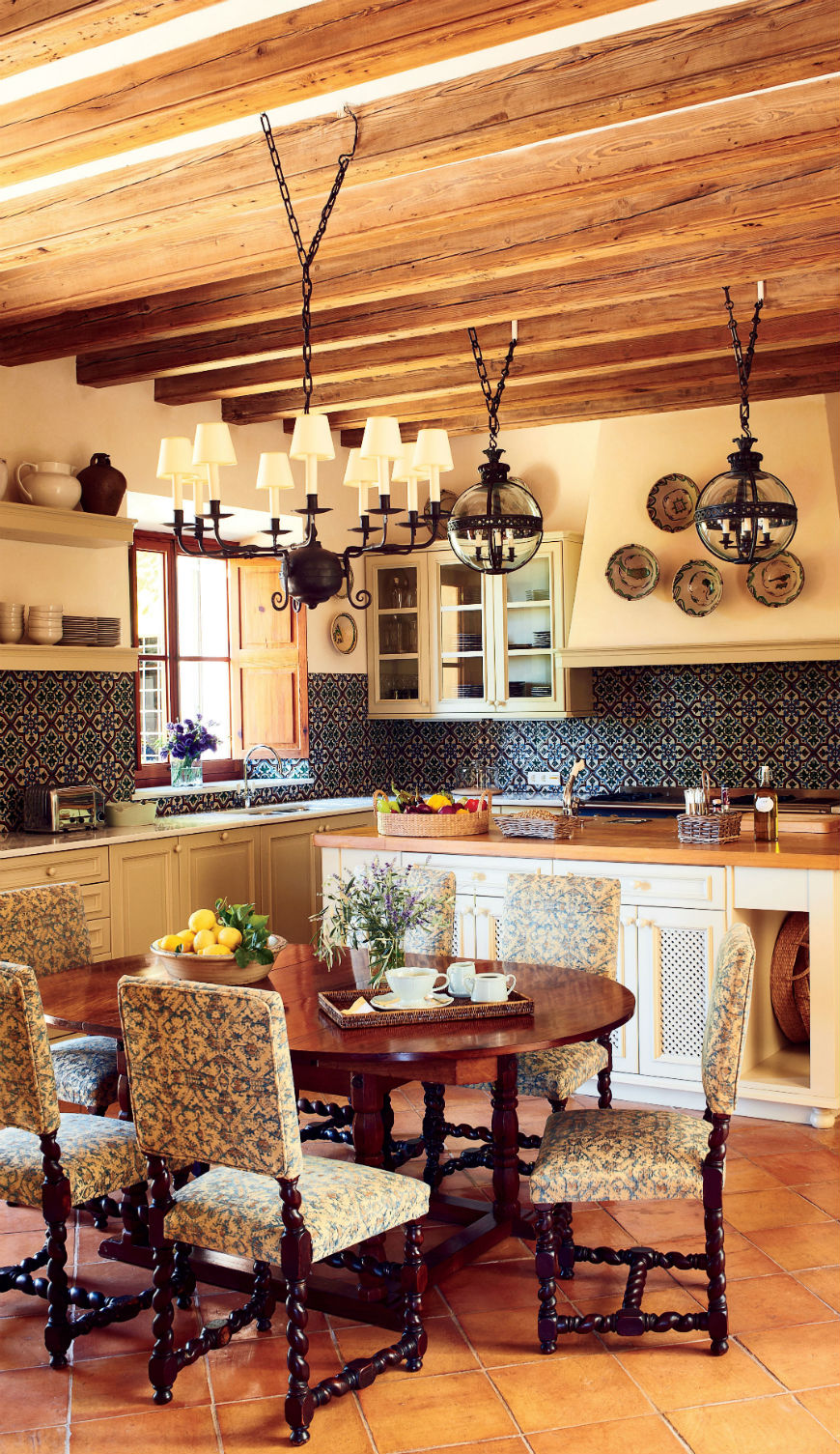 After: Designer Michael S. Smith added custom-made Moorish-style tile in the kitchen, where antique oak dining chairs surround an Indian table; the chandelier and the globe lights give a rustic look to the kitchen design.