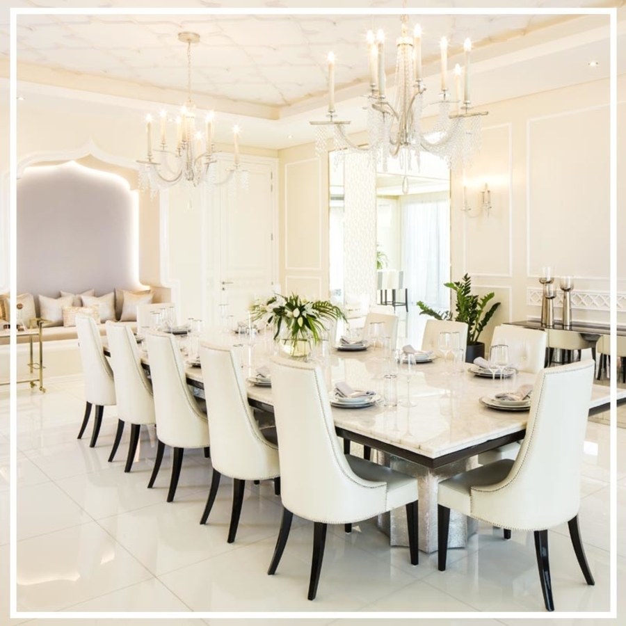 A white dining room with a white marble dining table complemented with several white leather dining chairs.