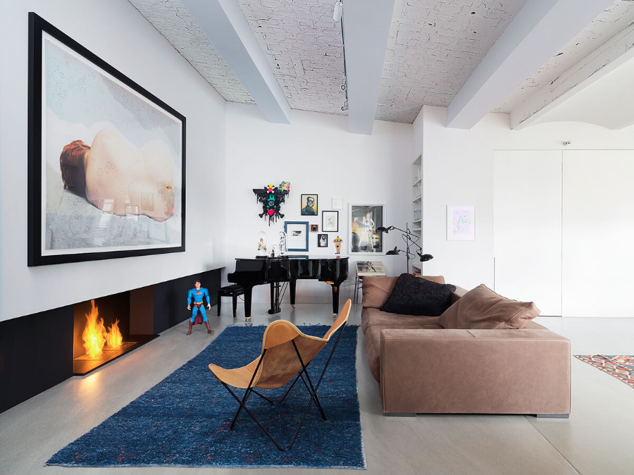 Photographer's loft with a terracotta sofa, one blue rug, a black piano, a fireplace, and a yellowish chair.