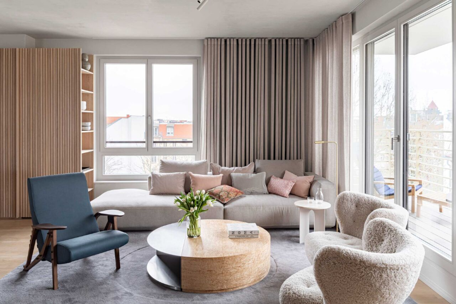 The Kastle interior design idea lliving room with 2 fluffy white armchairs, a round wood cente rtable, a blue leather-like armchair and a white/grey sofa.