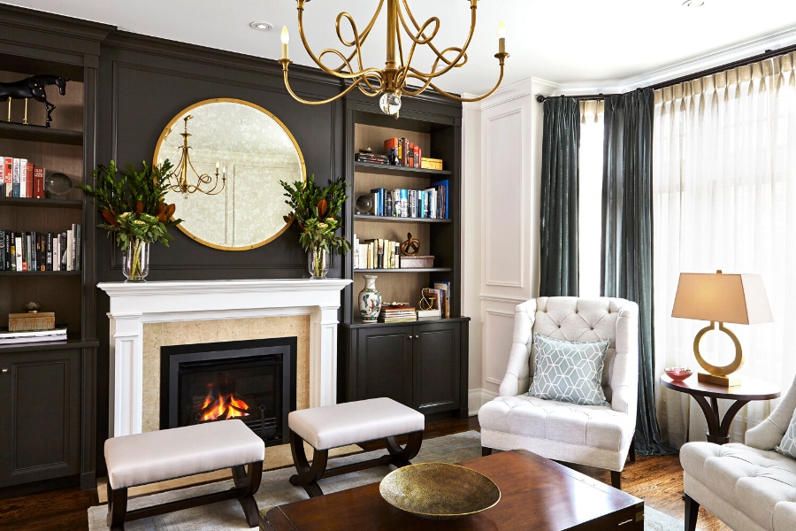 House decorating ideas by Laura Stein Interiors. This living room with a black wall with black shelves has a fireplace in white, a white armchair, two white benches, and a coffee table in wood.