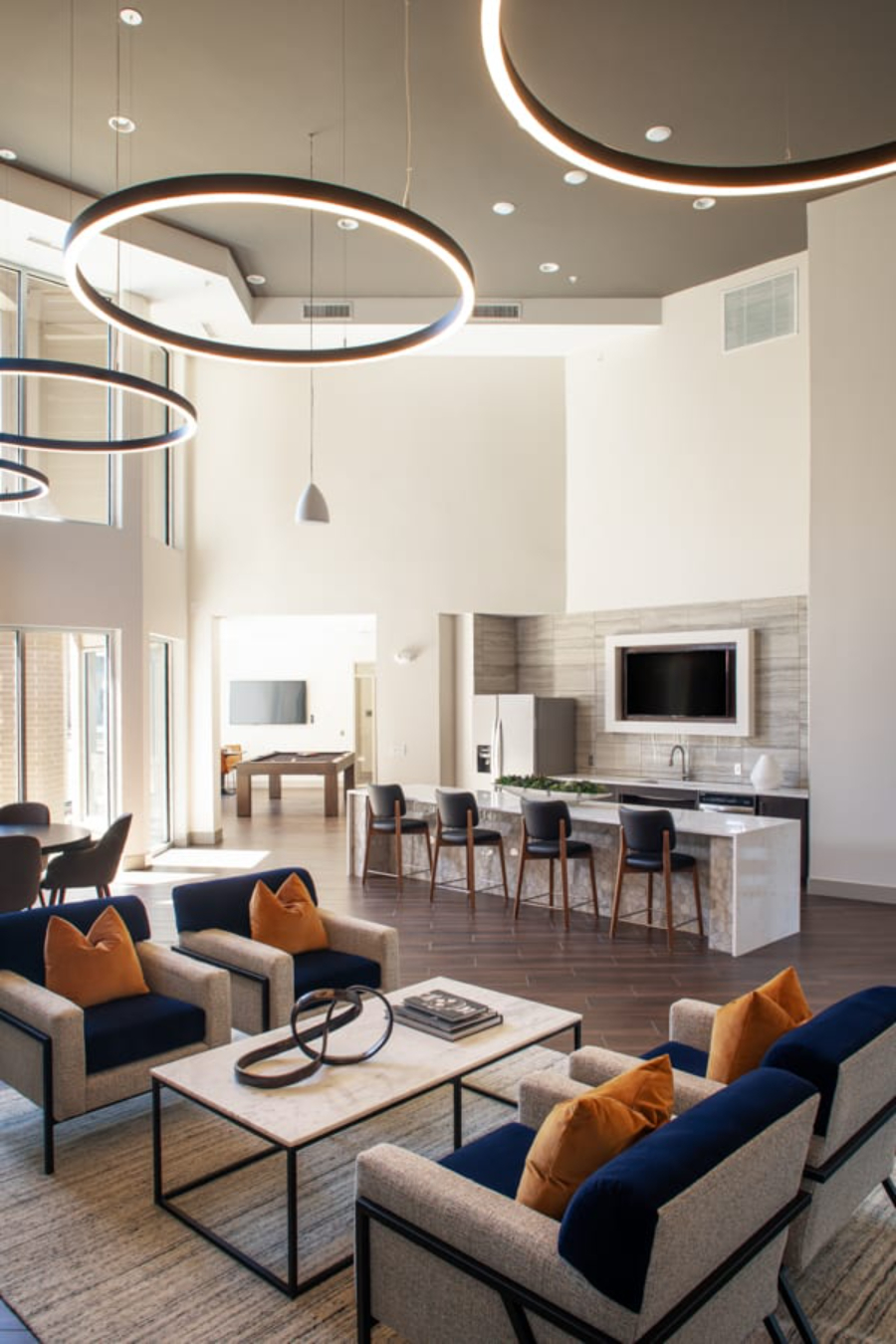 SJL Design Group: Interior Design In Texas. In this open space area there is a lounge area, a kitchenette, and there's a billiard room we can see in the background. On the main living area, there are four huge circular suspension lights.